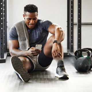 Fitness enthusiast sitting in a modern gym setting, tying his shoelaces next to a kettlebell, symbolizing strength training and dedication to a healthy lifestyle.